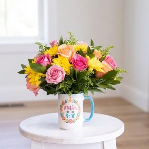 Mother of the Year mug arrangement with pink and peach roses, yellow chrysanthemums, and greenery