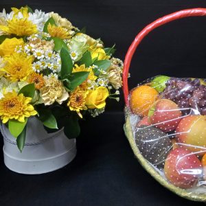 A festive gift set featuring a flower box with yellow and white blooms and a fresh fruit basket filled with an assortment of seasonal fruits.