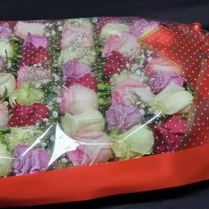 The Open Arms Bouquet showcases mixed roses in pink, red, and white shades, accented with baby’s breath, wrapped in starry cellophane, and tied with a red bow.