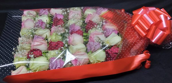 A luxurious bouquet of pink, red, and white roses, accented with baby’s breath, wrapped in transparent cellophane with star patterns, and tied with a bold red bow.