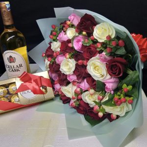 A luxurious gift set featuring a bouquet of red, white, and pink roses, a bottle of Cellar Cask wine, and a box of Ferrero Rocher chocolates.