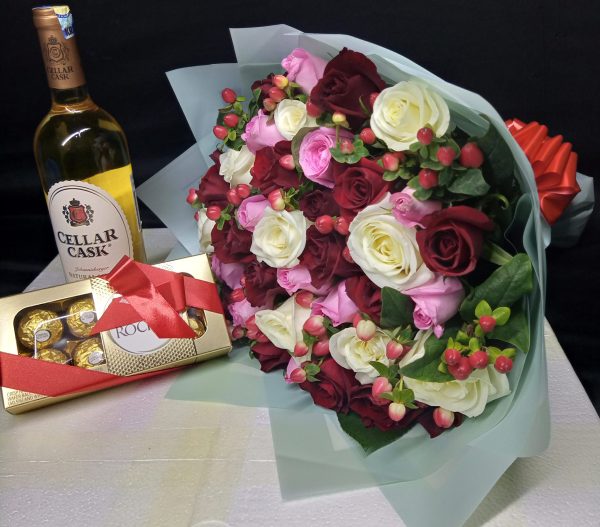 A luxurious gift set featuring a bouquet of red, white, and pink roses, a bottle of Cellar Cask wine, and a box of Ferrero Rocher chocolates.