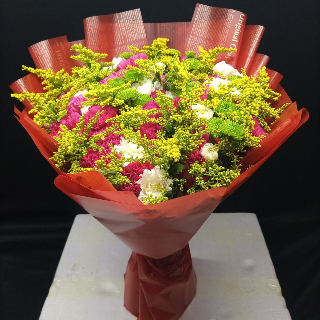 Friendly Petals bouquet of pink, white, and green carnations, accented with yellow fillers and wrapped in striking red paper.