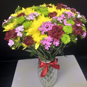 A vibrant vase arrangement featuring yellow daisies, green button chrysanthemums, and red and pink carnations, designed to brighten any space.