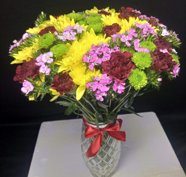 A vibrant vase arrangement featuring yellow daisies, green button chrysanthemums, and red and pink carnations, designed to brighten any space.